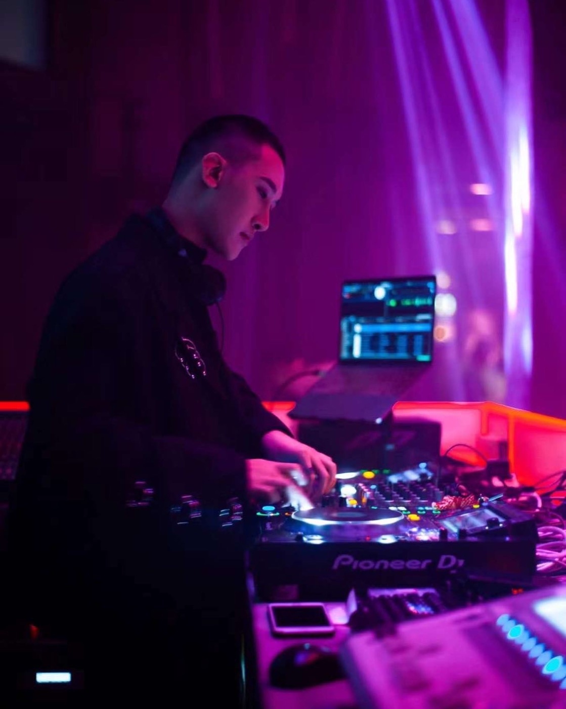 DJ 在活動現場操作 CDJ 打碟台,背景為光束燈效